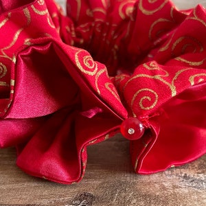 May include: Red fabric hair scrunchie with a gold swirl pattern and a red button with a clear rhinestone.