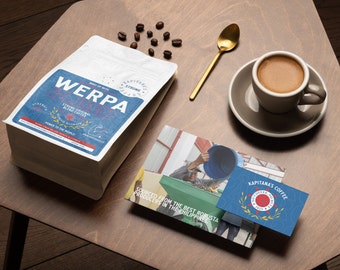 Könnte beinhalten: Ein brauner Papierbeutel mit einem blauen und weißen Etikett, auf dem "WERPA" und "Strong Original Blend Coffee" steht. Der Beutel liegt auf einem Holztisch mit einer Tasse Kaffee, einem Löffel und Kaffeebohnen.