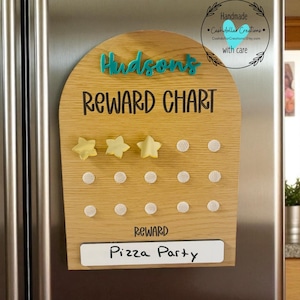May include: Wooden reward chart with the name "Hudson's" in teal letters. The chart includes the words "Reward Chart" and "Reward" in black. The reward is "Pizza Party". Includes three yellow star magnets.