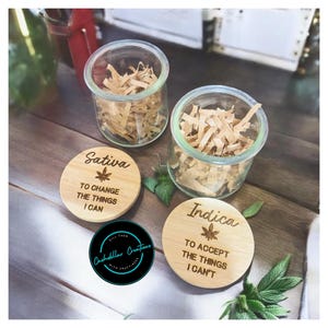 May include: Two wooden lids with engraved text and a leaf design. The lids read "Sativa To Change The Things I Can" and "Indica To Accept The Things I Can't".