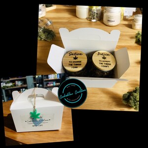 May include: A white box with a lid open, revealing two glass jars with wooden lids. The lids have the words "Sativa" and "Indica" written on them, along with a quote about changing and accepting things. The box is sitting on a wooden surface.