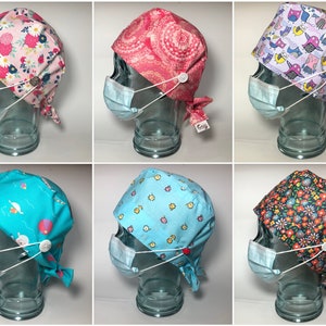 May include: Six different patterned surgical caps with ties and a button closure. The caps are displayed on glass mannequins with surgical masks.