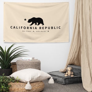 Puede incluir: Un tapiz de pared de lona beige con una silueta negra de un oso y el texto "CALIFORNIA REPUBLIC" y las coordenadas "36.7783° N, 119.4179° W".