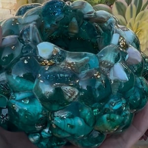 May include: Teal blue resin bowl with a bubbled texture and embedded seashells. The bowl is filled with gold glitter and white seashells.