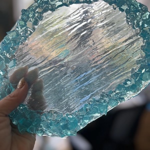 May include: A clear glass coaster with a textured surface and a border of small, turquoise blue glass pieces.