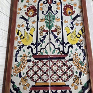 May include: A rectangular wall art piece consisting of four ceramic tiles set in a brown wooden frame. The tiles feature a symmetrical design of two yellow birds perched on dark blue branches above a patterned vase with orange and green floral motifs.
