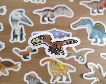 May include: A collection of dinosaur stickers, featuring various species in cartoon style. The stickers are white-bordered and include a brown and tan raptor, a blue Spinosaurus, and other colorful prehistoric creatures. The stickers are scattered on a light brown surface.