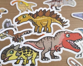 May include: A collection of colorful dinosaur stickers. The stickers feature various dinosaurs in cartoon style, including a T-Rex, Stegosaurus, and others. The dinosaurs are in shades of green, yellow, brown, and red, with white outlines.