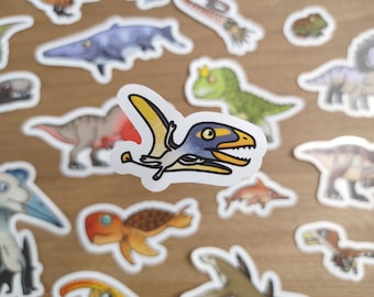 May include: A collection of dinosaur stickers, featuring a cartoon pterodactyl with yellow wings, a blue head, and an open mouth. Other dinosaur stickers are visible in the background, including a green dinosaur and a long-necked dinosaur.