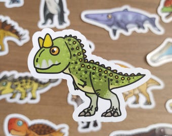 May include: A collection of colorful dinosaur stickers. The stickers feature various dinosaur illustrations in shades of green, brown, orange, and blue. The stickers are outlined in white and are on a wooden surface.
