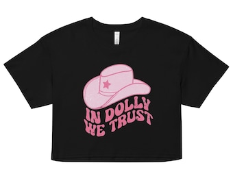 Può includere: Maglietta nera a maniche corte con un cappello da cowboy rosa e il testo "In Dolly We Trust" in un font retrò.