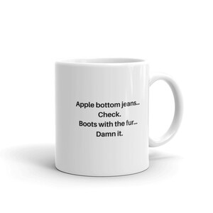 May include: White ceramic mug with black text that reads "Apple bottom jeans... Check. Boots with the fur... Damn it."