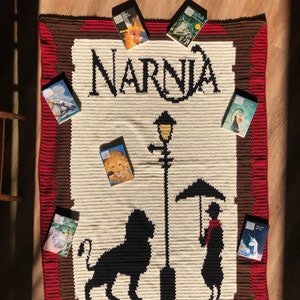 May include: A crocheted blanket with a brown and red border featuring a silhouette of a lion and a person holding an umbrella. The blanket has the word "Narnia" in black yarn. Seven books with covers featuring characters from the Narnia series are arranged around the blanket.