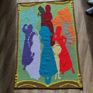 May include: A crocheted wall hanging with a framed design of multiple figures in various colors, including purple, blue, red, orange, and brown.