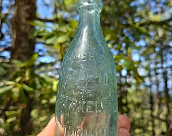 May include: A clear glass bottle with a rounded bottom and a narrow neck. The bottle has embossed text that reads "W.S. 1240 SPARKLES TORONTO".