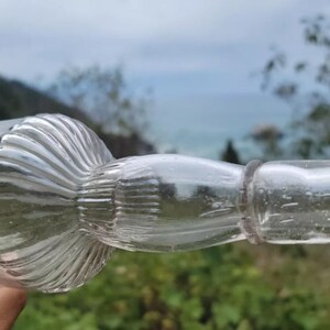 May include: A clear glass bottle with a textured, fluted design. The bottle has a round, bulbous base and a long, thin neck.