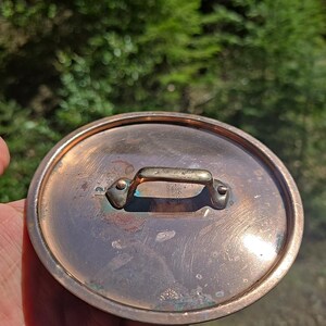 May include: Copper pot lid with a brass handle. The lid has a slightly tarnished finish and shows signs of use.