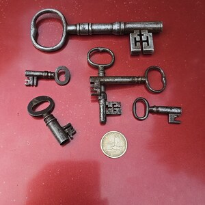 May include: A collection of six antique keys, some with intricate designs, on a red surface. A gold coin is also visible in the image.