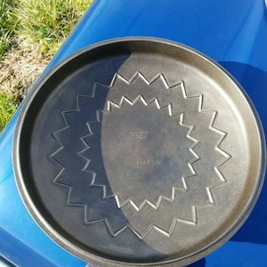 May include: A black cast iron skillet with a starburst pattern on the bottom. The skillet is 10 inches in diameter and has a smooth, black finish.