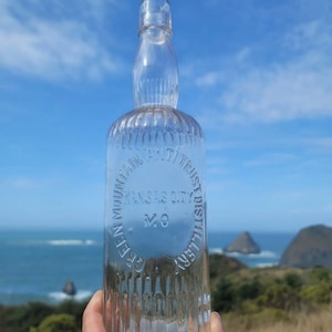 May include: A clear glass bottle with a textured surface. The bottle has a circular label that reads "Green Mountain Bottling Trust Kansas City Mo Distillery".