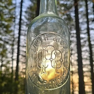May include: A clear glass bottle with a textured surface. The bottle has a label that reads "Roth & Co. San Francisco".