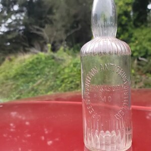 May include: A clear glass bottle with a textured surface. The bottle is labeled "Seven Mountain Ant Trust Distillery Kansas City MO".
