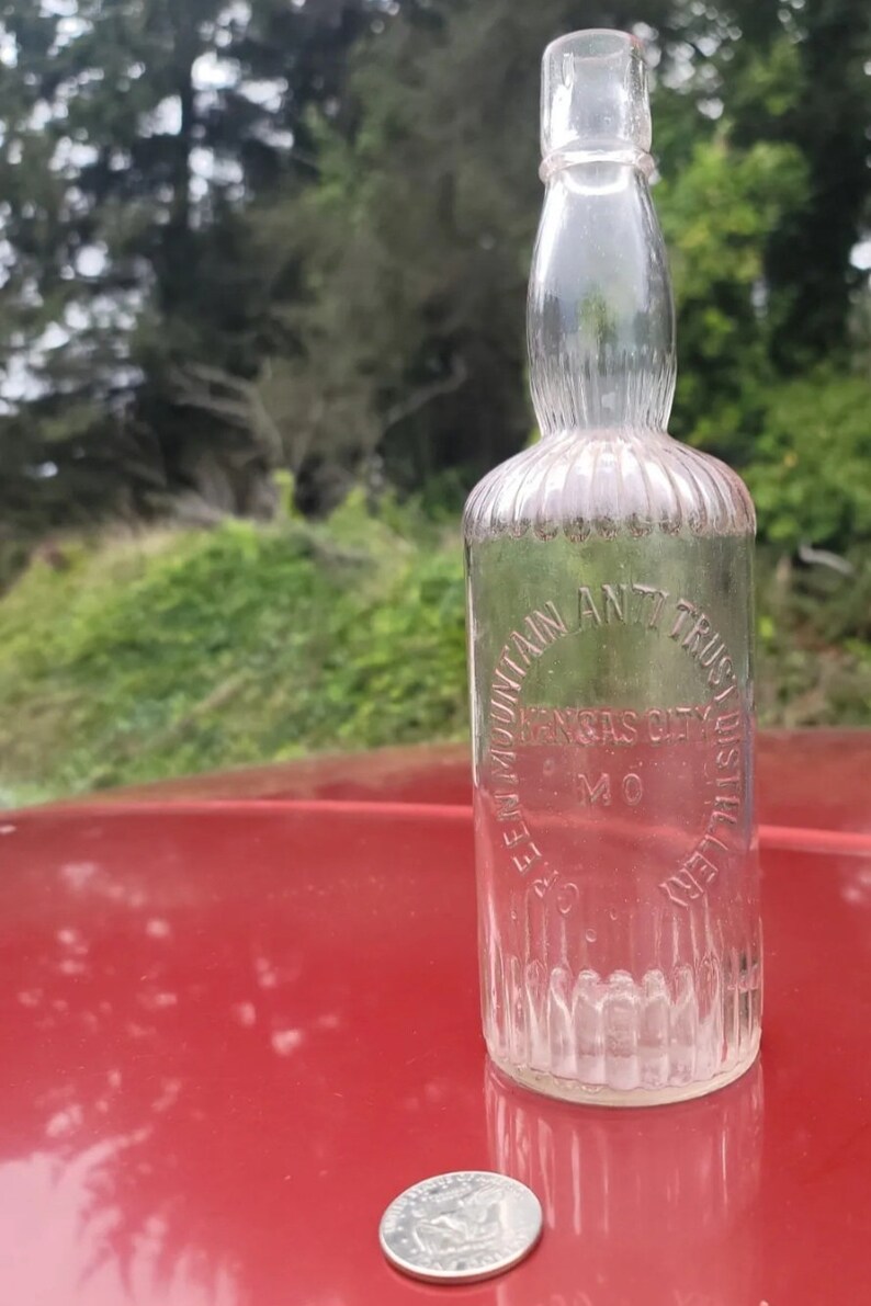 May include: A clear glass bottle with a textured surface. The bottle is labeled "Seven Mountain Ant Trust Distillery Kansas City MO".