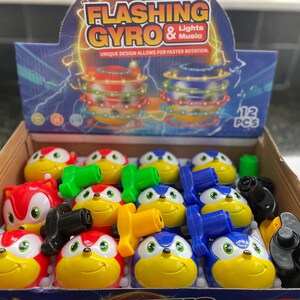 May include: A box of 12 flashing gyro toys. The toys are in red, blue, and yellow colors with a cartoon character design. The box has the words 'Flashing Gyro & Lights Music' and 'Unique design allows for faster rotation' printed on it. The box also has a picture of a flashing gyro toy.