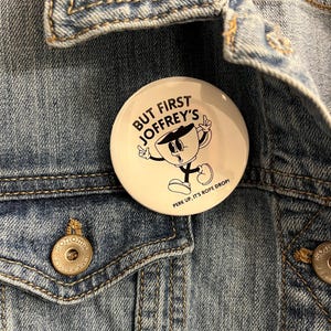 May include: A white button with black text and a cartoon coffee cup. The text reads "But First Joffrey's" and "Perk Up. It's Rope Drop!"