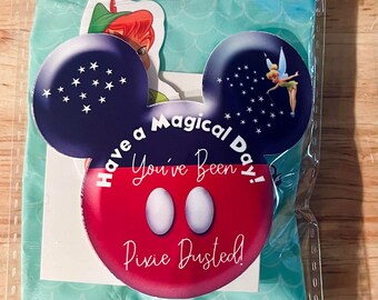 May include: A clear plastic package containing Disney-themed stickers. The main sticker is Mickey Mouse-shaped with the text "Have a Magical Day! You've Been Pixie Dusted!" Other stickers include Peter Pan and Tinkerbell. The package has a teal mermaid scale pattern.