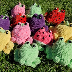 May include: A collection of crocheted frog plushies in various colors and fruit designs, including watermelon, strawberry, and pineapple. The plushies are made with soft yarn and have embroidered eyes and mouths.