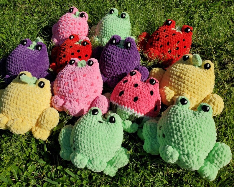 May include: A collection of crocheted frog plushies in various colors and fruit designs, including watermelon, strawberry, and pineapple. The plushies are made with soft yarn and have embroidered eyes and mouths.