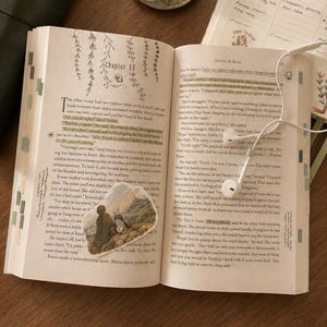 May include: An open book with a decorative sticker, a weekly planner with handwritten notes and a deer illustration, a brass candlestick with a white candle, white wired earbuds, and two pens. The book page shows Chapter 14 and text.