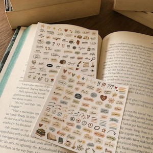 Può includere: Due fogli di adesivi rettangolari con piccole icone colorate ed etichette di testo per annotare i libri. I disegni includono stelle, cuori, frecce, libri, tazze di caffè e vari termini letterari come tema, metafora e prefigurazione.