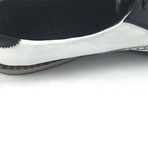 May include: Close-up of the white leather toe of a black and white leather oxford shoe. The shoe has a brown rubber sole.