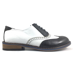 May include: White and black leather oxford shoes with a wingtip design and a brown sole.