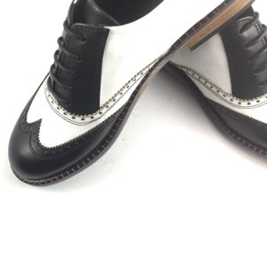 May include: Black and white leather oxford shoes with a wingtip design and a brown stitched sole.