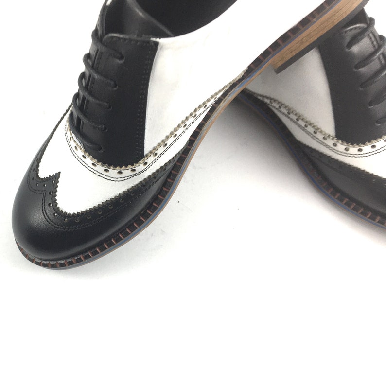 May include: Black and white leather oxford shoes with a wingtip design and a brown stitched sole.