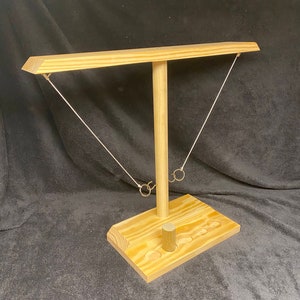 May include: Wooden ring toss game with a tall post and a horizontal beam. The base has six holes for the rings to land in.