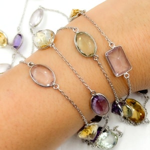 May include: A silver chain bracelet with multiple gemstone charms. The charms are in various shapes and colors, including clear, light pink, light green, and purple.