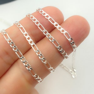 May include: Four silver chains of different lengths and widths, displayed on a hand.
