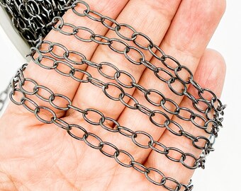 Op de afbeelding: Vijf strengen zwarte ketting in verschillende maten, getoond op een hand. De ketting is gemaakt van metaal en heeft een matte afwerking.