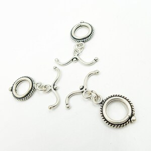 May include: Three silver-toned metal clasps with a rope-like design around the circular part. Each clasp has a hook on one end and a loop on the other.