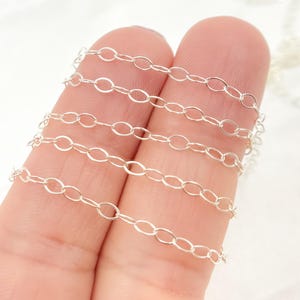 May include: Five silver chains of different lengths and thicknesses, held between two fingers.