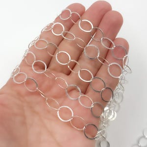 May include: Silver chain with oval links. The chain is made of small, interconnected oval-shaped links, creating a delicate and modern look.