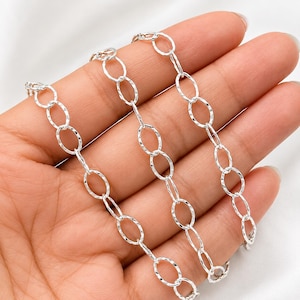 May include: A silver-toned metal chain featuring a series of interconnected oval-shaped links. Each individual link displays a textured, hammered surface finish that reflects light, creating a consistent pattern throughout the entire length of the chain.