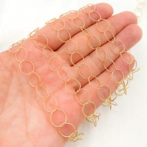 May include: Gold chain with a delicate, twisted oval link design. The chain is shown in a hand, highlighting the intricate details of the links.