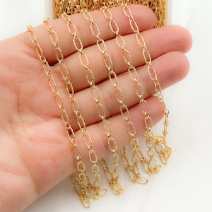 May include: A close-up of a gold chain with a textured oval link design. The chain is displayed on a hand, showing the length and detail of the links.