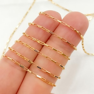 Op de afbeelding: Een close-up van een gouden ketting met een box chain-ontwerp. De ketting wordt in meerdere lengtes getoond, met de uiteinden van de ketting rustend op een vinger.