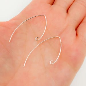 May include: Two silver earring hooks, also known as ear wires, are shown on a hand. The hooks are made of thin, smooth wire and have a simple, elegant design.